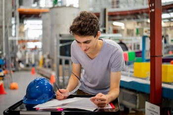 Studierender liest Arbeitsanweisungen in der Werkhalle