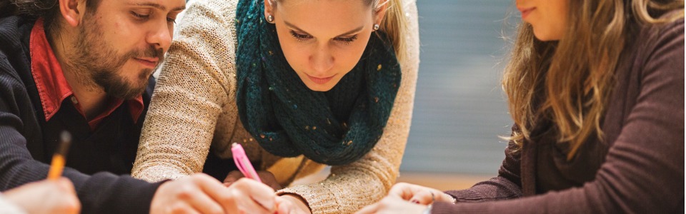 Drei erwachsene Studierende arbeiten an einem Tisch zusammen an einer Studienaufgabe