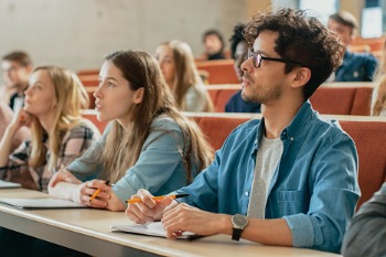 Studierende sitzen in einem Hörsaal ihrer Hochschule und verfolgen die Vorlesung.