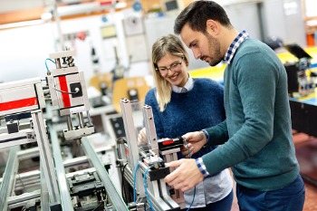 Zwei dual Studierende arbeiten in ihrem Betrieb an einer mechanischen Anlage