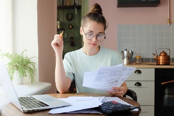 Junge Frau mit Brille geht am Schreibtisch ihre Unterlagen für die Studienfinanzierung durch