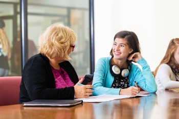 Eine Studentin sitzt mit einer Studienberaterin an einem großen Holztisch und unterhält sich mit ihr.