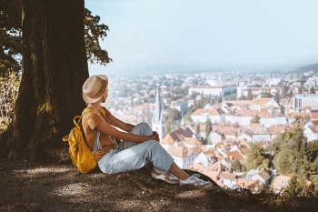 Eine junge Frau sitzt auf einem Hügel und überblickt von dort aus das Stadtpanorama