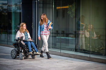 Studentin im elektrischen Rollstuhl auf Campus